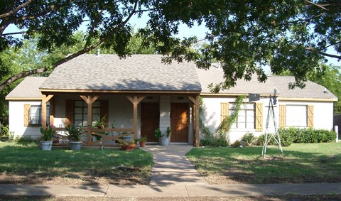 A house with a covered front porch and a tree in front.